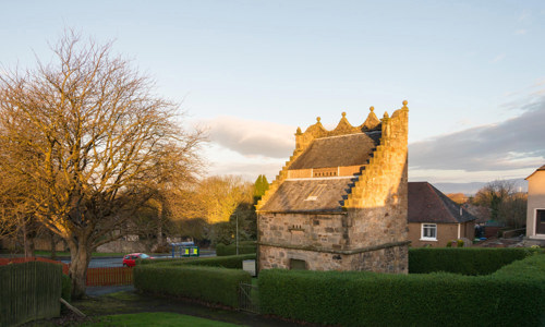 The very complete Westquarter dovecot is surrounded by a hedge and trees.