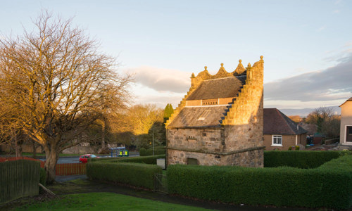 The very complete Westquarter dovecot is surrounded by a hedge and trees.