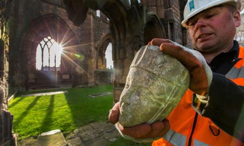 A staff member holding a carved head at Elgin Cathedral, one of many pieces of stonework on display in a new exhibition.