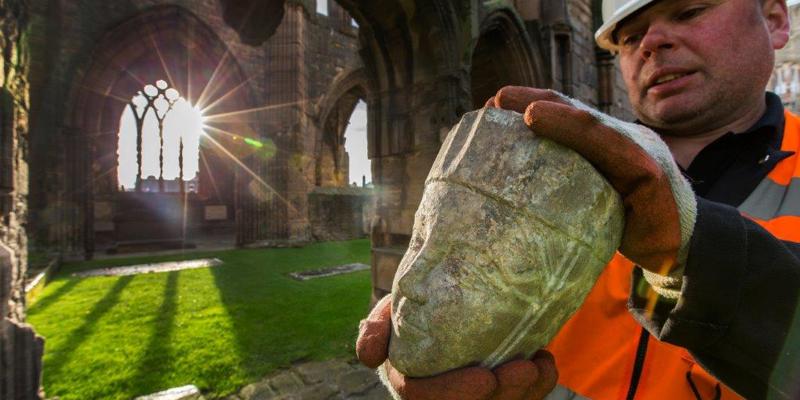 A staff member holding a carved head at Elgin Cathedral, one of many pieces of stonework on display in a new exhibition.