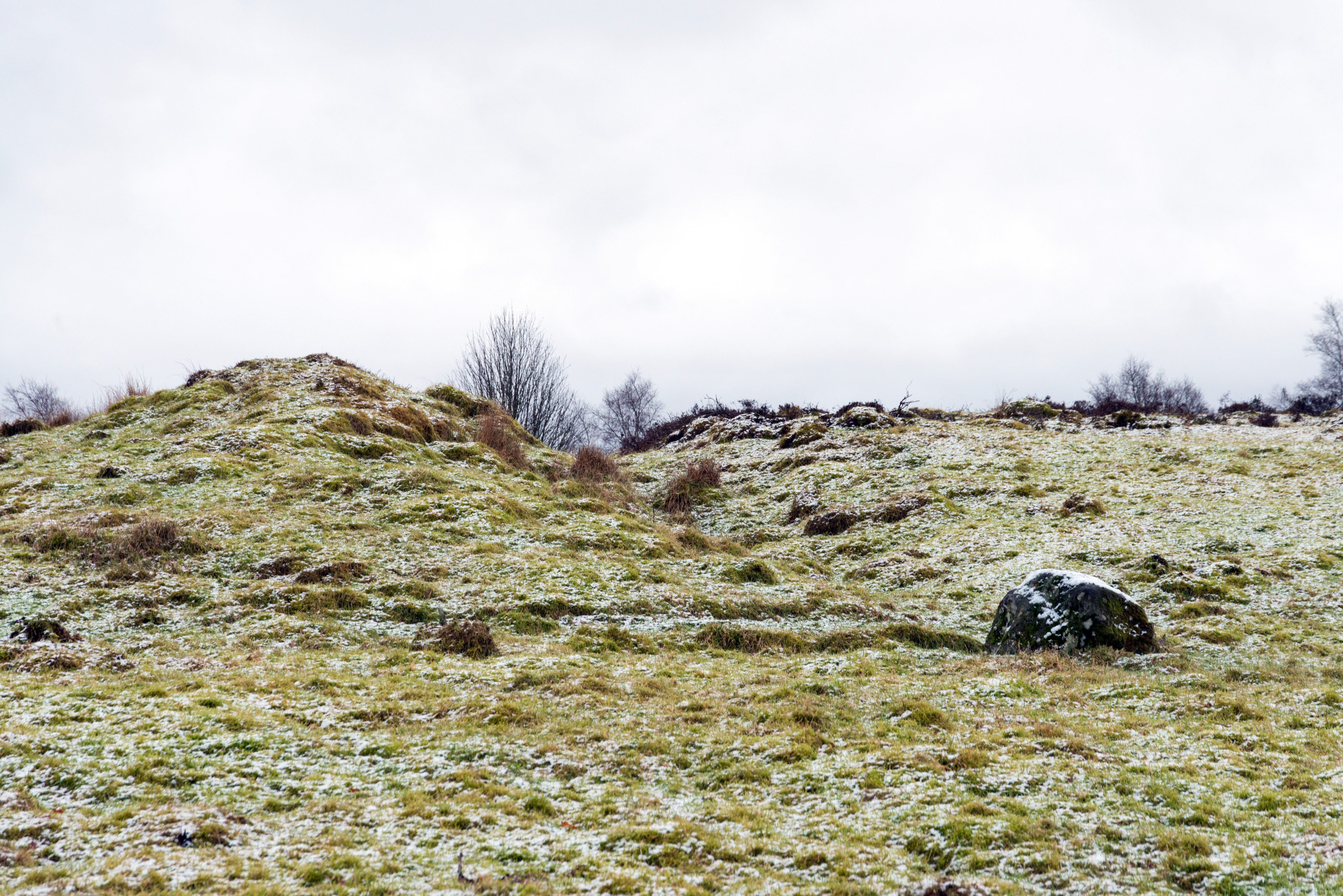 A snow speckled, rocky field with two small manmade hills