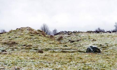 A snow speckled, rocky field with two small manmade hills