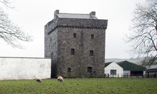 A dark square tower house surrounded by a few white modern buildings