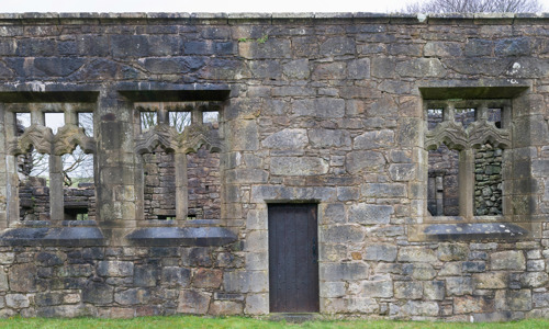 A stone facade with three large windows and a small wooden door