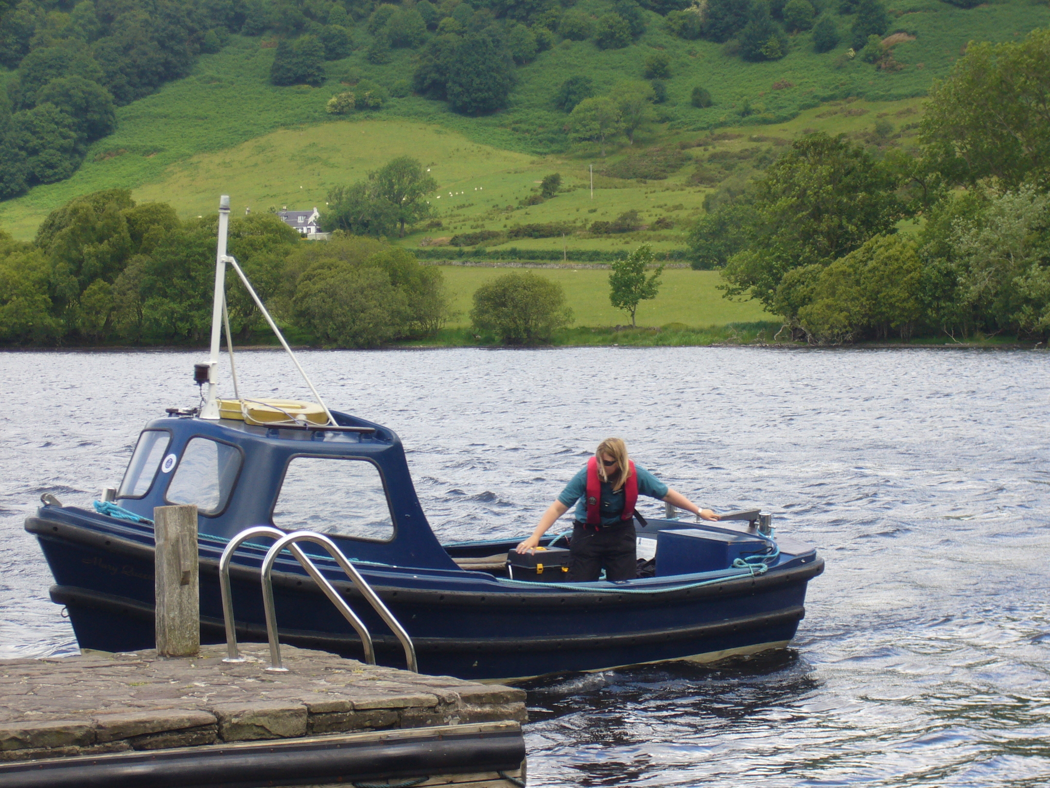 A Historic Scotland staff member in a lifejacket using a tiller to dock a small boat at a stone jetty