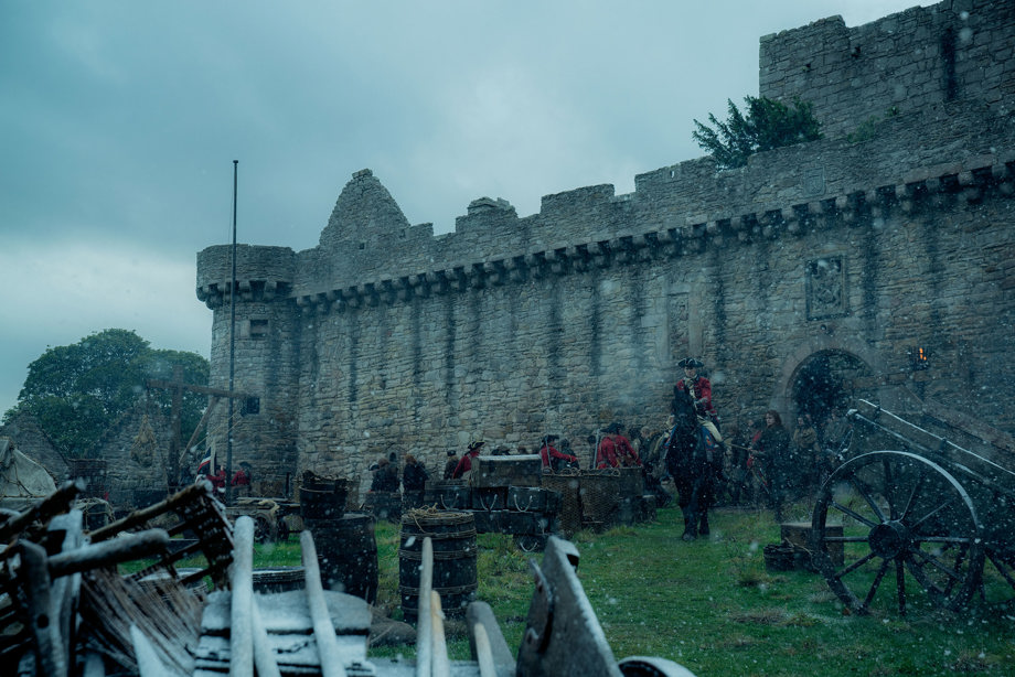 A scene outside a castle with soldiers, horses, trebuchet and barrels 