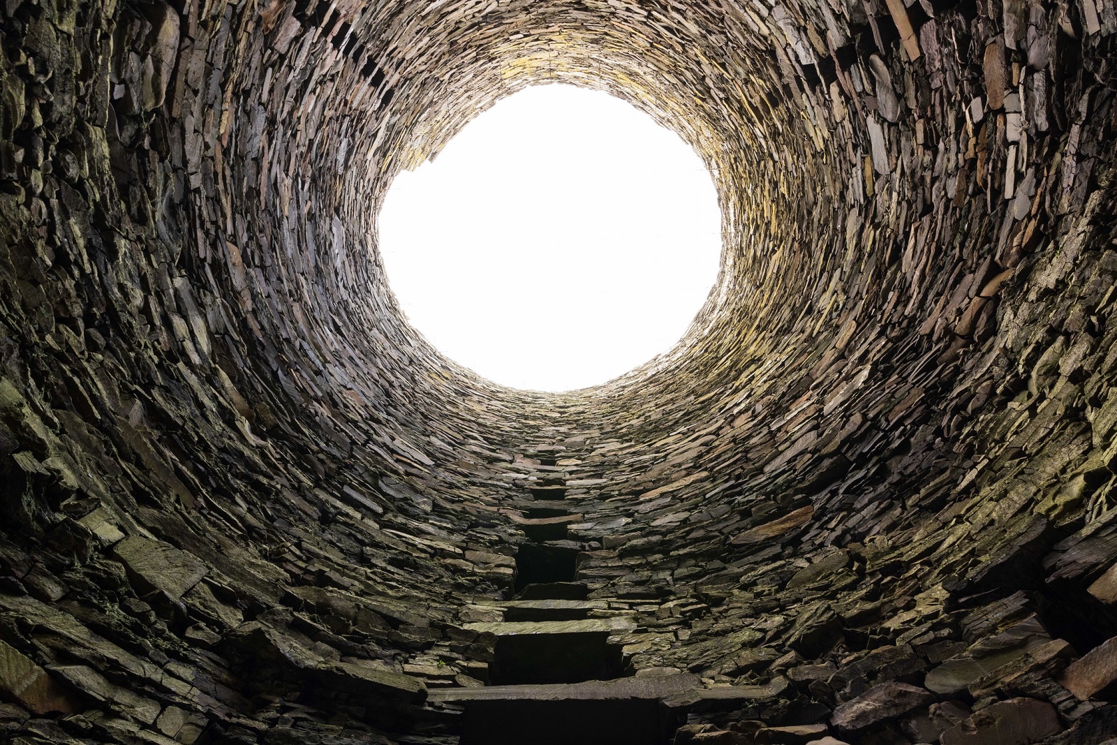 Interior view looking straight up inside Mousa Broch, showing the conical stone walls tapering toward a bright circular opening at the top.