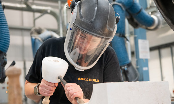 A woman wearing a safety helmet and gloves carving into stone