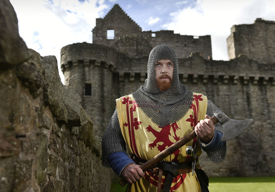 A man in chainmail holding an axe standing in the grounds of a castle 
