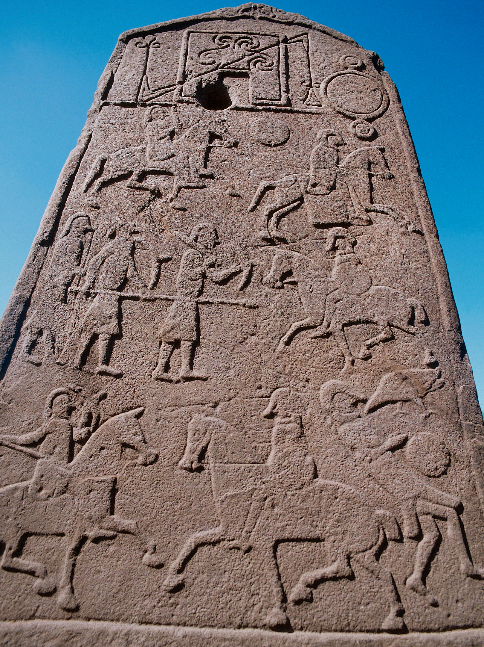 A close-up shot of carvings on a Pictish stone showing men on horseback, possibly involved in a battle.