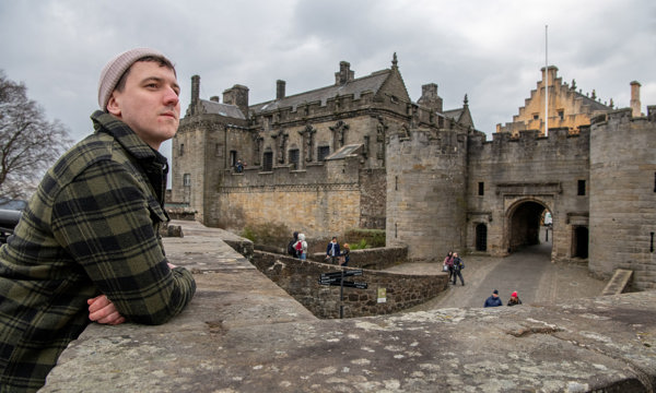 A man wearing a checked shirt and hat leaning on a brick wall overlooking the Queen Anne Garden at Stirling Castle