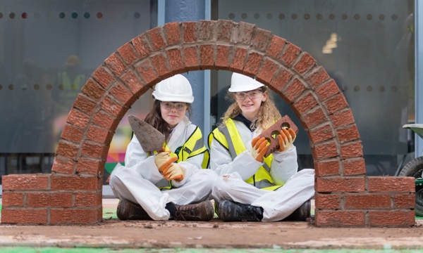 Two Glasgow school children sit with a brich archway they built during a traditional skills workshop.