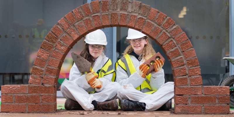 Two Glasgow school children sit with a brich archway they built during a traditional skills workshop.
