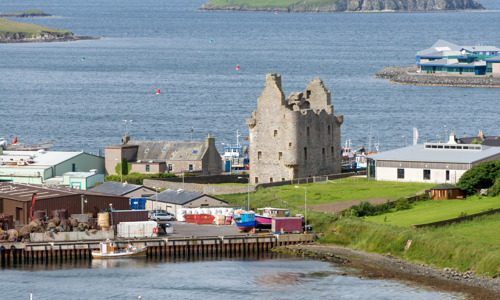 Scalloway Castle seen from a distance, surrounded by more modern houses and boats