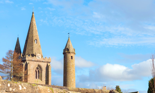 A tall but narrow roundtower reaching into the sky next to a traditional church tower