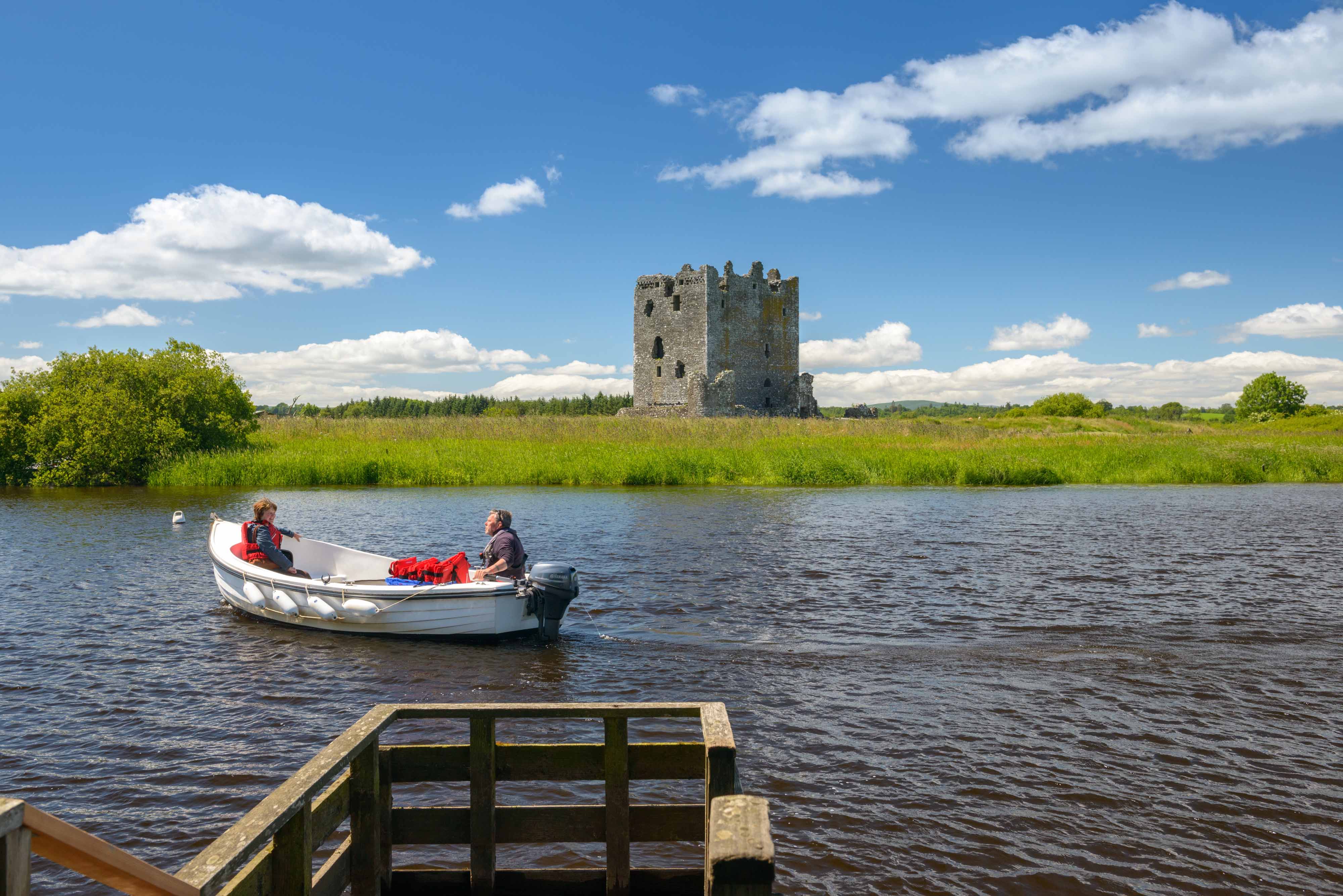 Two people on a rowing boat on a stretch of water in front of a lonely stone castle