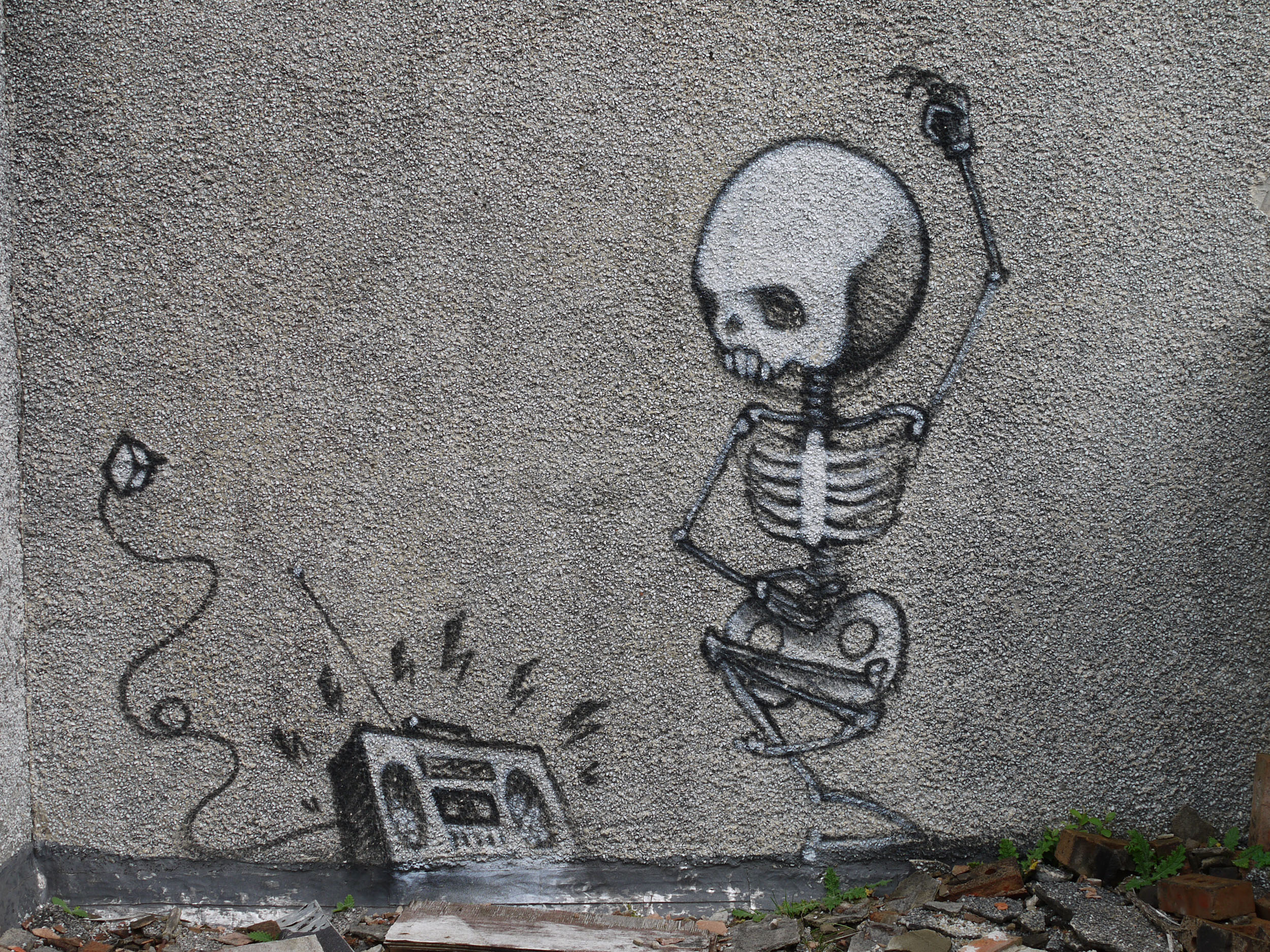 An image of graffiti on a grey wall. The graffiti shows a skeleton dancing music from a boombox
