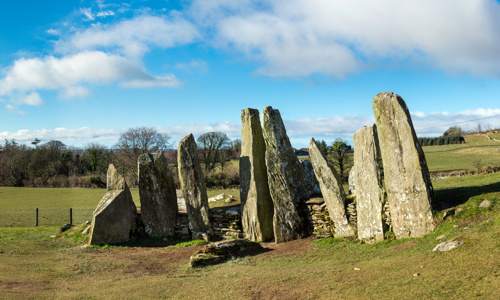 About eight thin standing stones stand side by side on a field