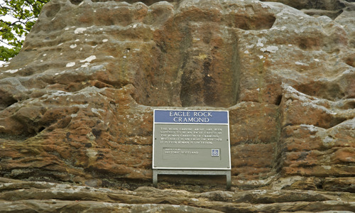 The weather-worn carving of an eagle on a large rockface. In front of it is an interpretation sign
