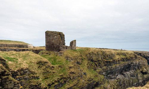 A cliff by the sea, on top of which the small ruin of the Castle of Old Wick stands