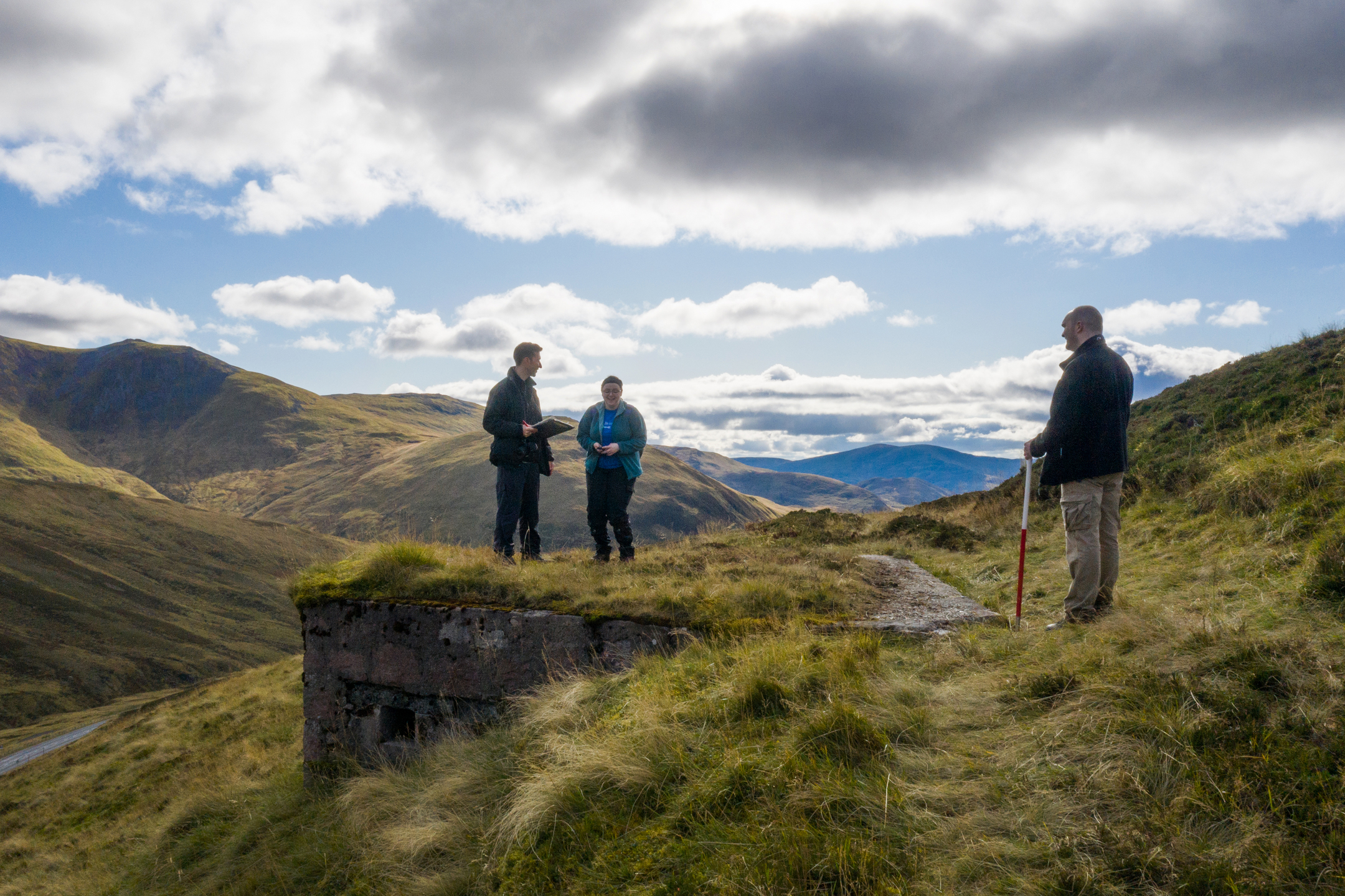 Three HES employees survey ruins of World War Two defenses in front of dramatic Highland scenery. 
