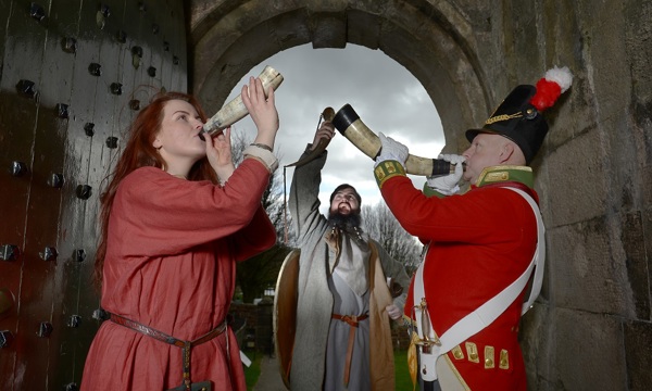 Three re-enactors blowing horns under an archway