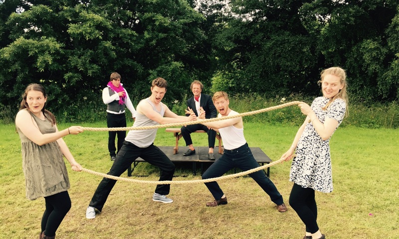 A group of theatre students outdoors on some grass posing with a rope