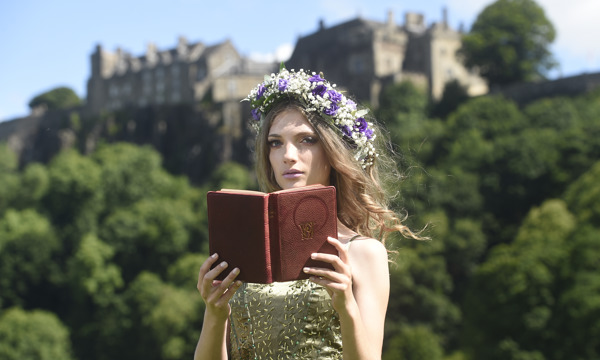 Actress holding a brown book, wearing a wreath hair piece with Stirling Castle in the background