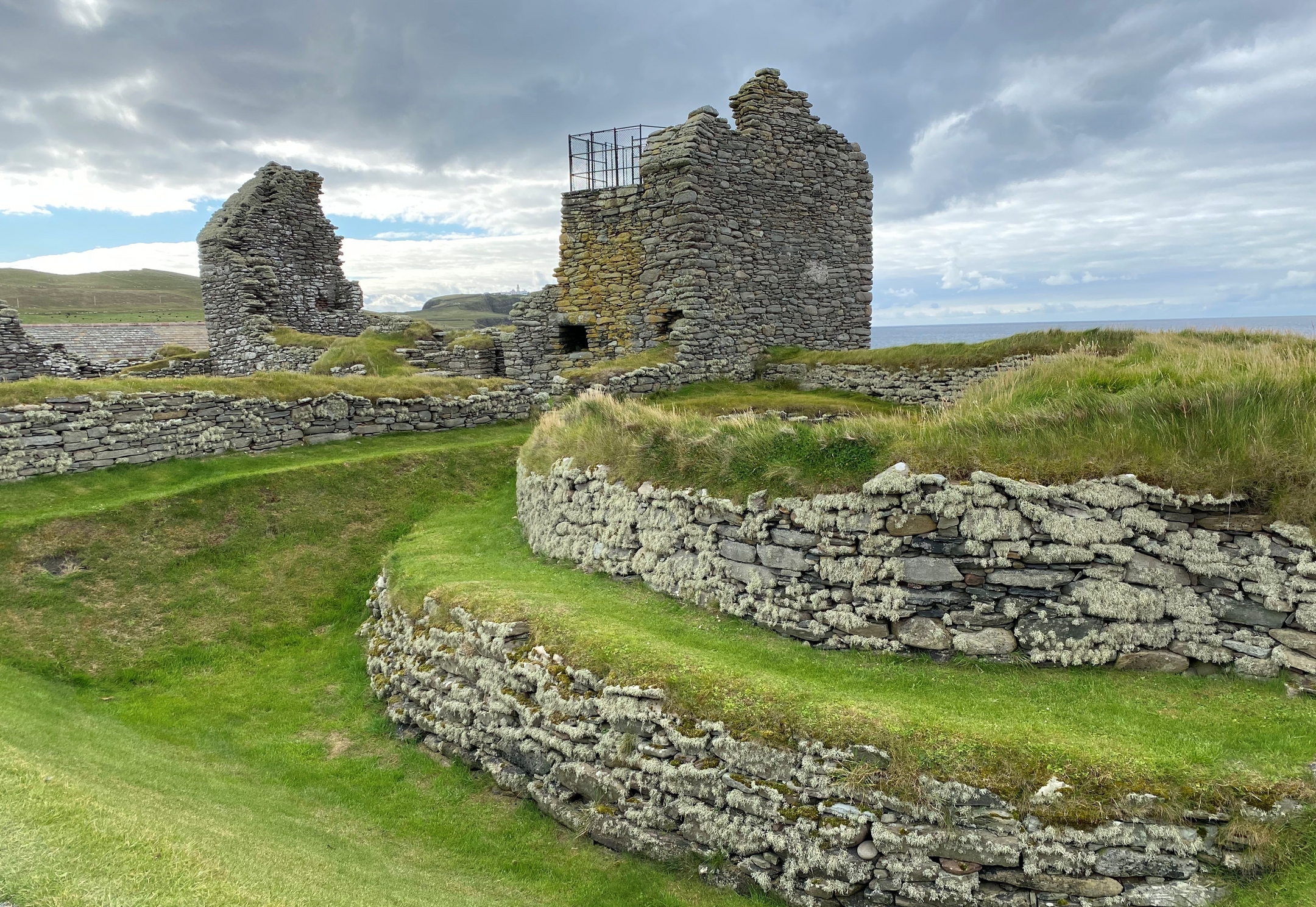 Stone walls with grass embankments on top and the ruins of a house structure