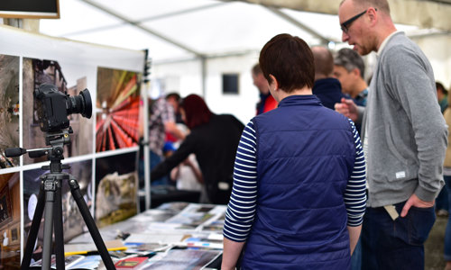 Two people standing next to a camera on a tripod on a table at an exhibition