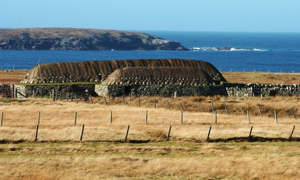 Distant photo of The Blackhouse at Arnol with fields in the foreground and the North Atlantic Ocean in the background