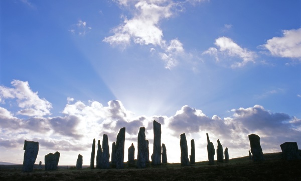 Calanais Standing Stones with sun breaking through a small gathering of clouds behind the stones