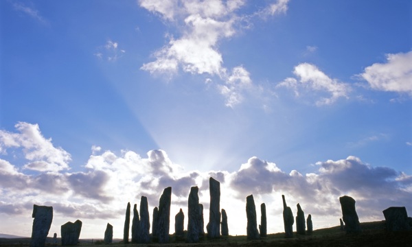Calanais Standing Stones with sun breaking through a small gathering of clouds behind the stones
