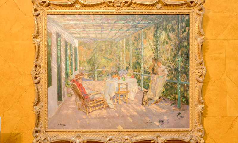 A photogaph of a painting of people sitting and standing in a pergola