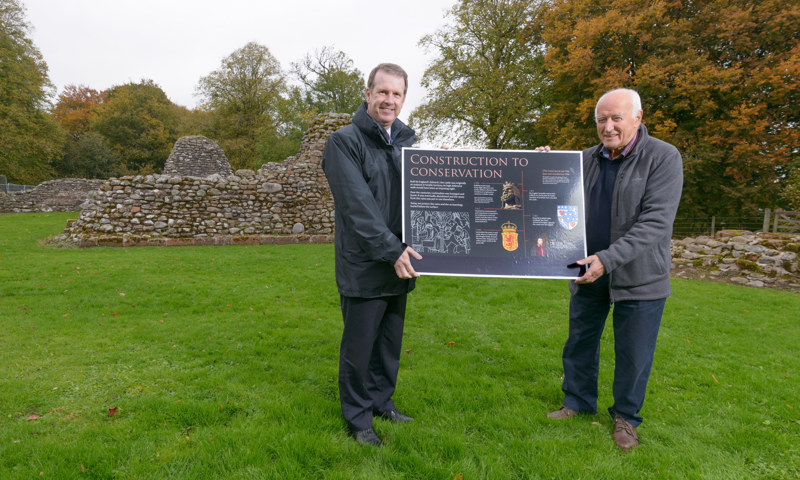 Two men in a park holding a sign headed "Construction to Conservation"