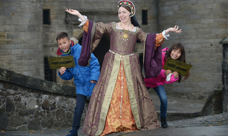 A woman in a re-enactment costume with two children behind her holding out Golden Tickets