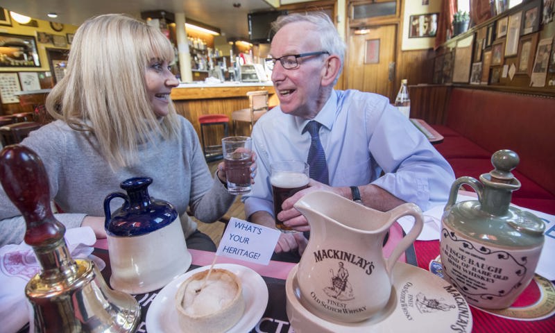 Two people talking in a cafe with teapots, a bell, and a pie with a flag in it that says "What