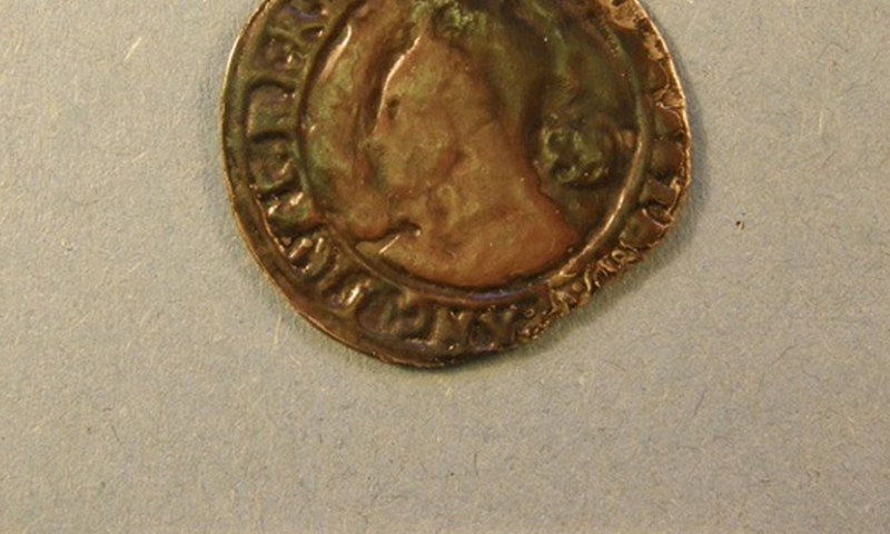 An old coin, pictured with a small measure for scale.