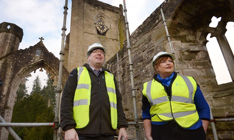 A photograph of a man and a woman stood in high visibility jackets and wearing white hard hats