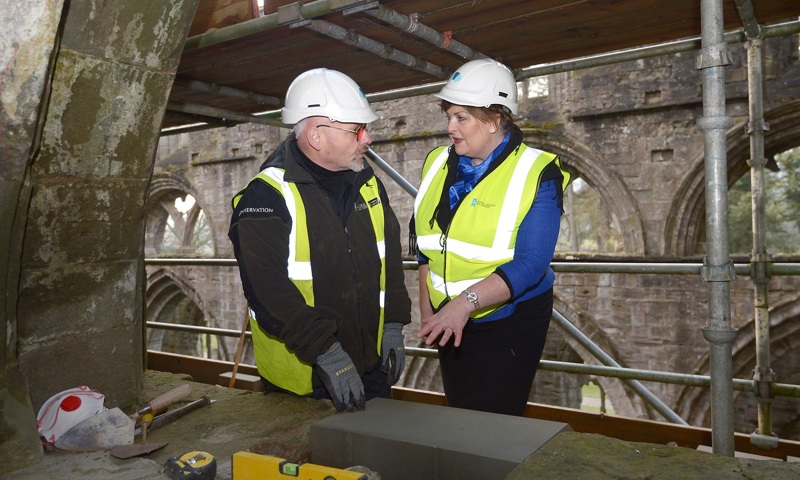 A photograph of a man and a woman stood in high visibility jackets and wearing white hard hats