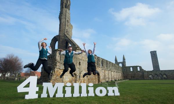 Three members of staff at St. Andrew's Cathedral leaping in the air above a large 3D sign that reads "4 Million"