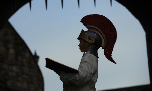 Side view of a child at Edinburgh castle wearing a roman centurian's helmet holding an open book
