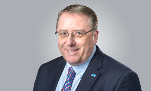 A man in a suit and tie, wearing glasses, smiling at the camera