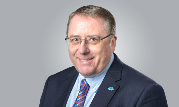 A man in a suit and tie, wearing glasses, smiling at the camera