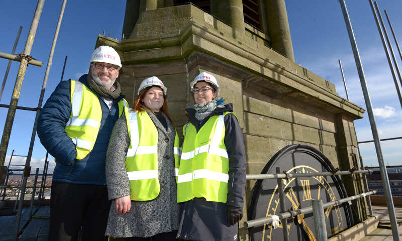 Three people in hard hats and high visibility vests on scaffolding at the top of The Falkirk Steeple