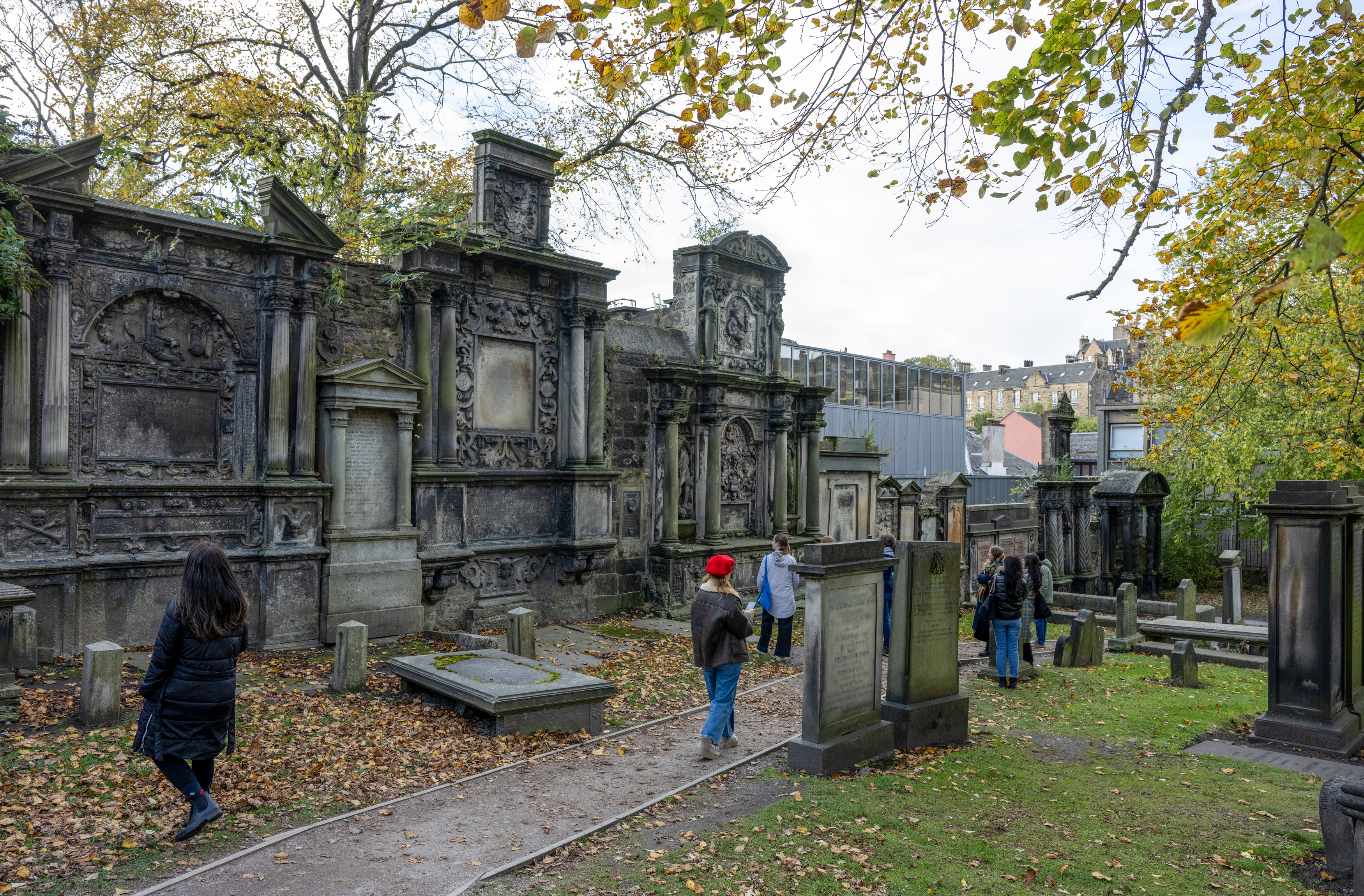 It is an sunny, early autumn day in Edinburgh's Greyfriars Kirkyard Cemetery, and a group of people are walking through the grounds looks at some of the stonework.