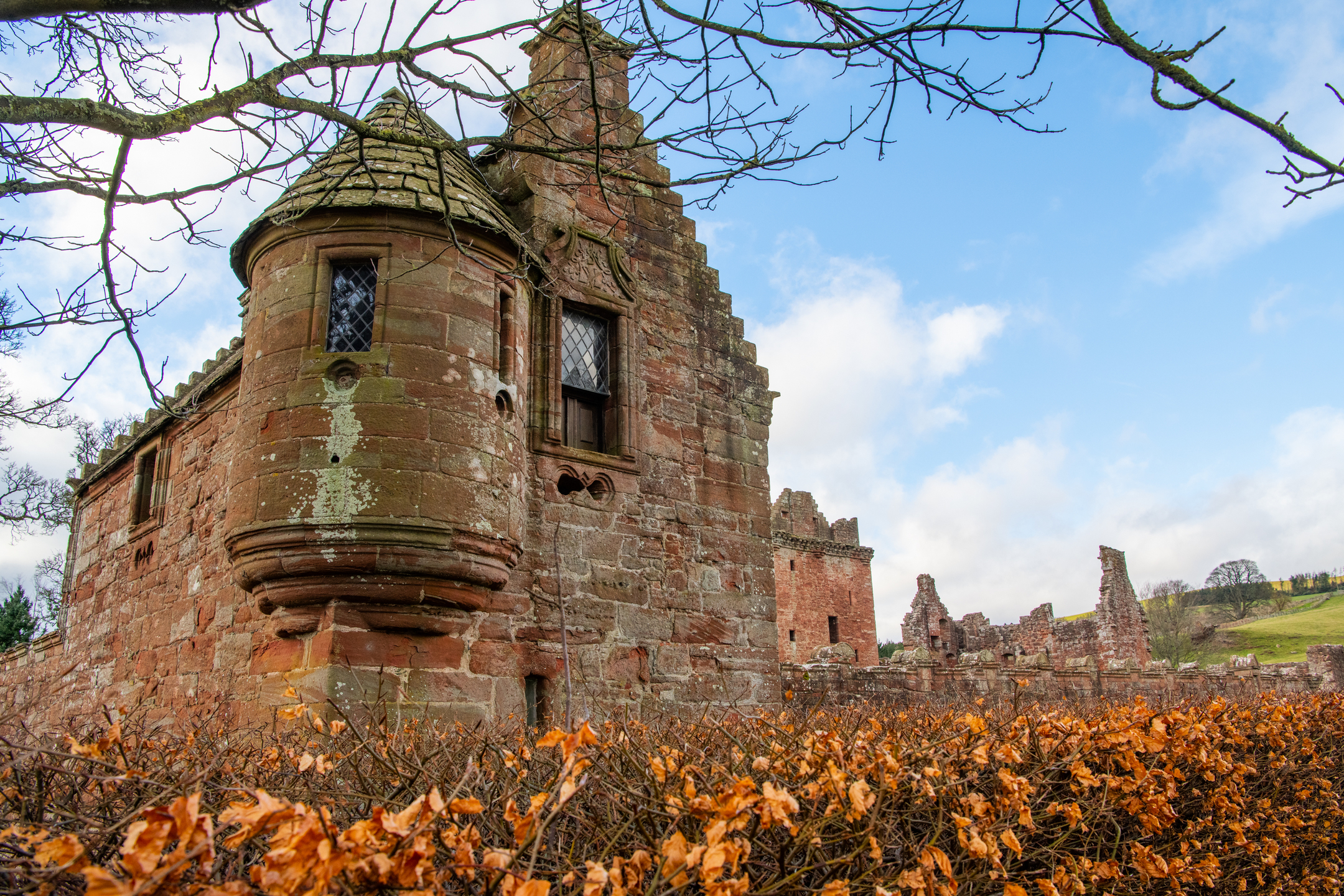 A small stone building with a circular tower and stepped gables. It forms part of a castle complex. More ruinous towers and turrets are in the background. 