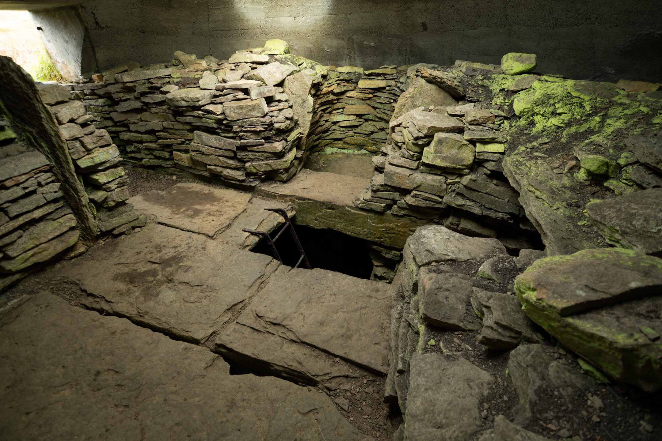 Inside view of cairn with stone floor and walls and passageway in floor