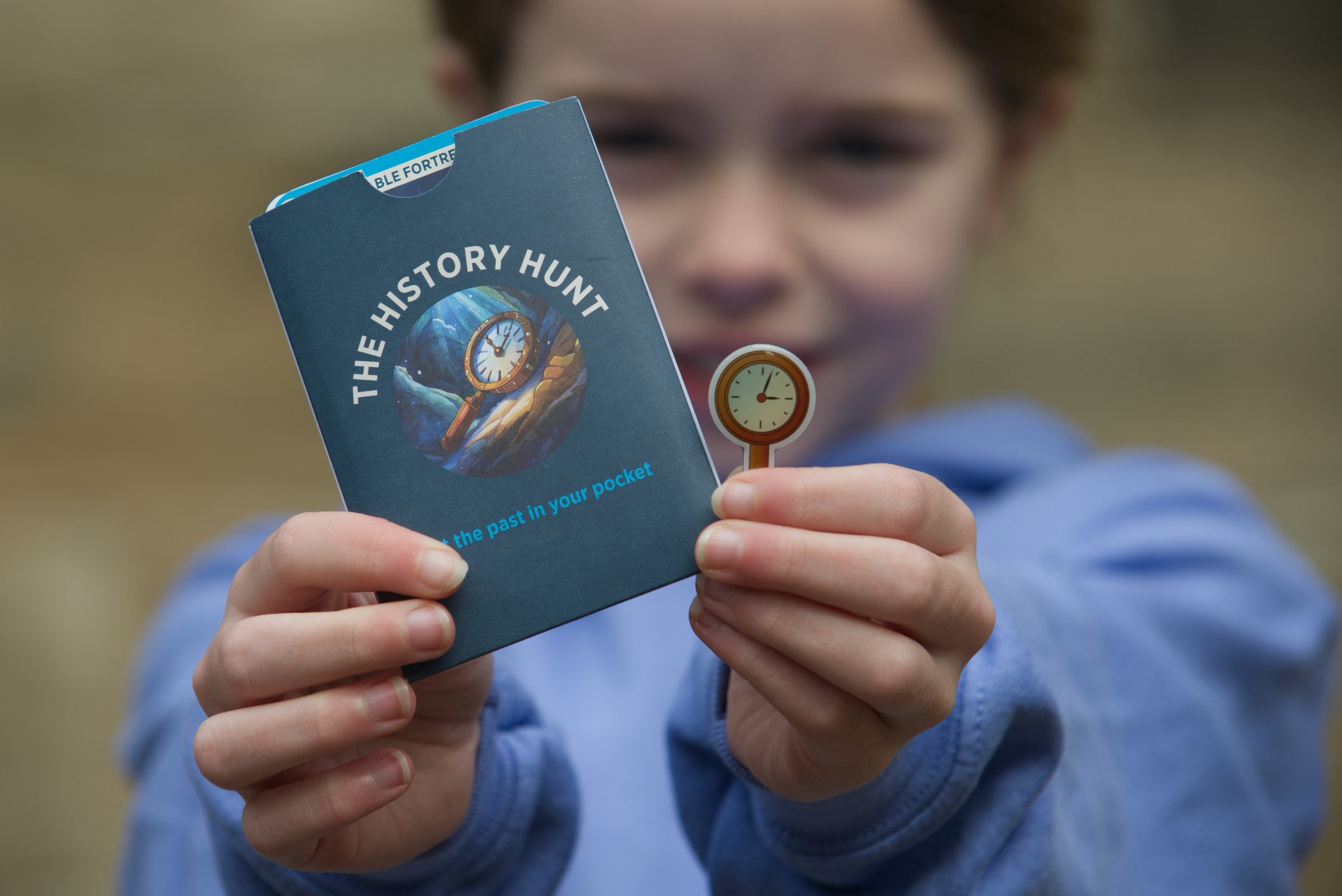 A child holds up a sleeve designed for holding "history hunt" playing cards and a special pin badge awarded to those who have collected all the cards.