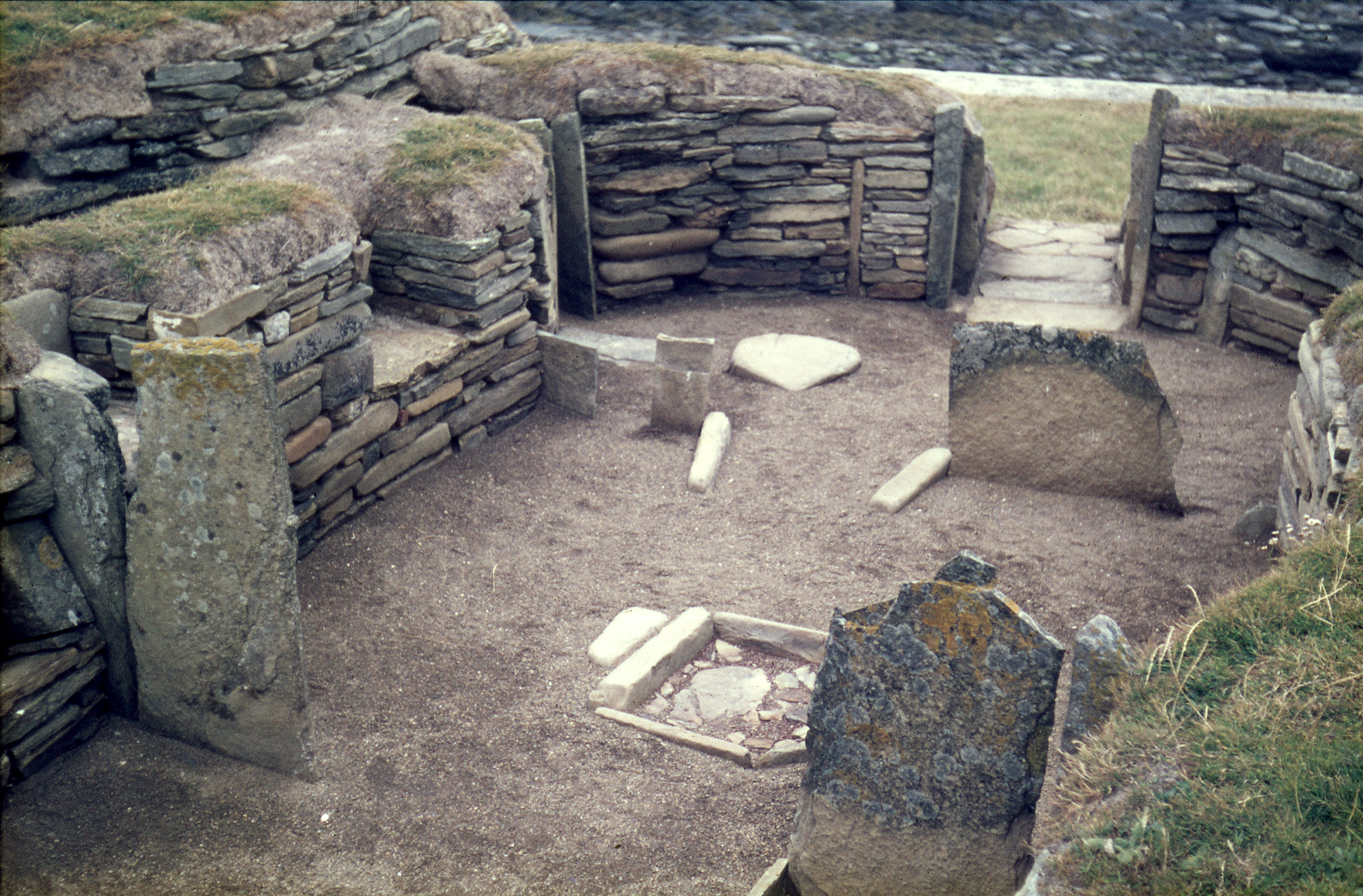 Inside the stone-walled chamber of the Knap of Howar, showing flat stone slabs and hearth-like features set into a dirt floor